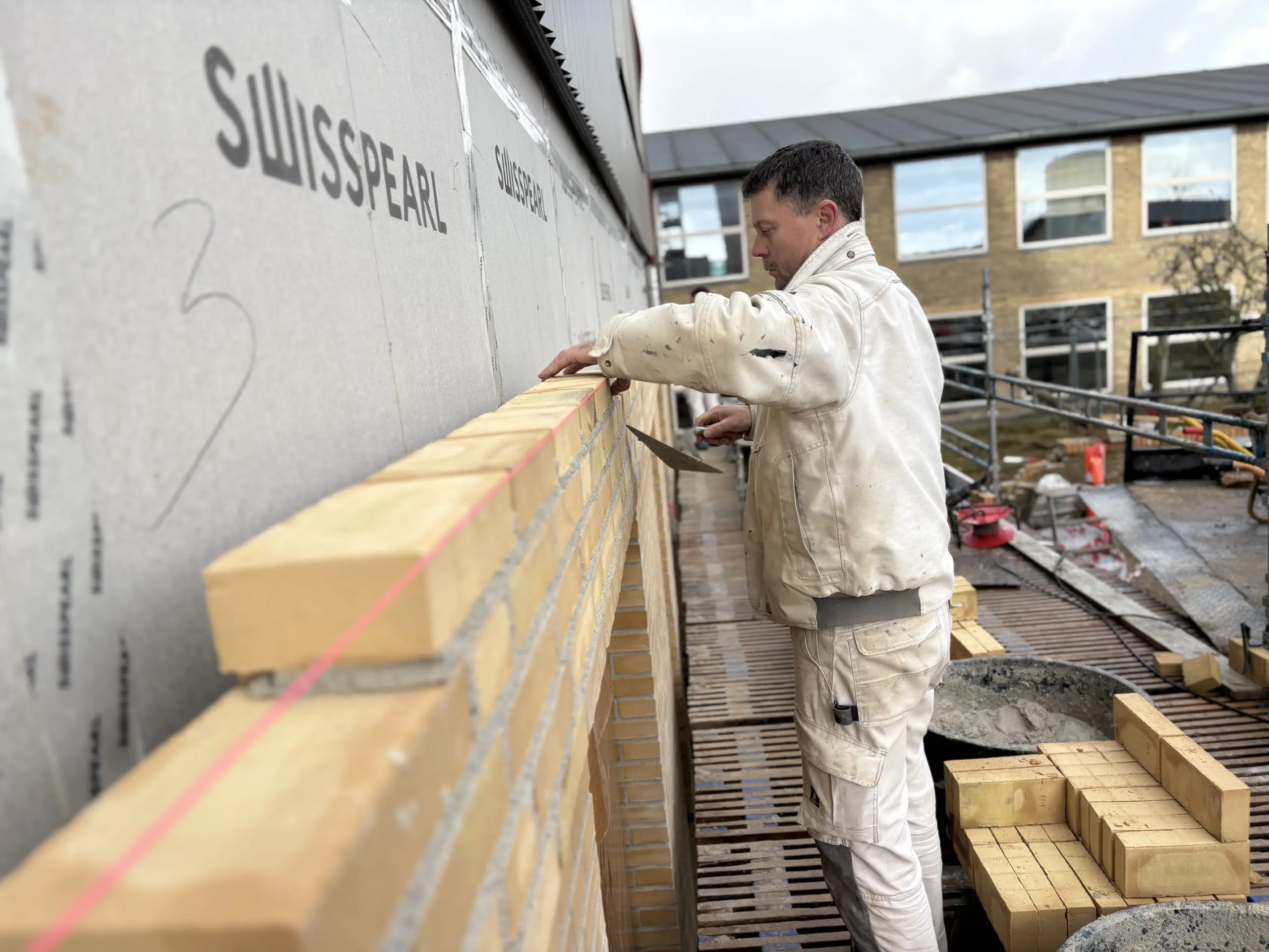 En murer fra Ole Sommer A/S udfører præcis skalmuring med gule mursten på en byggeplads.