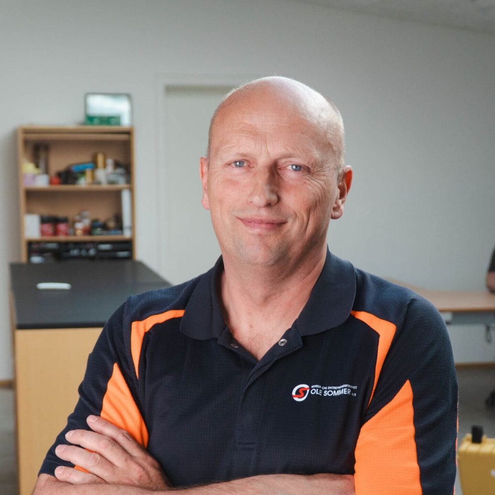 Portræt af Kenneth Reichstein Hansen fra Ole Sommer A/S iført arbejdstøj med logo og armene over kors.