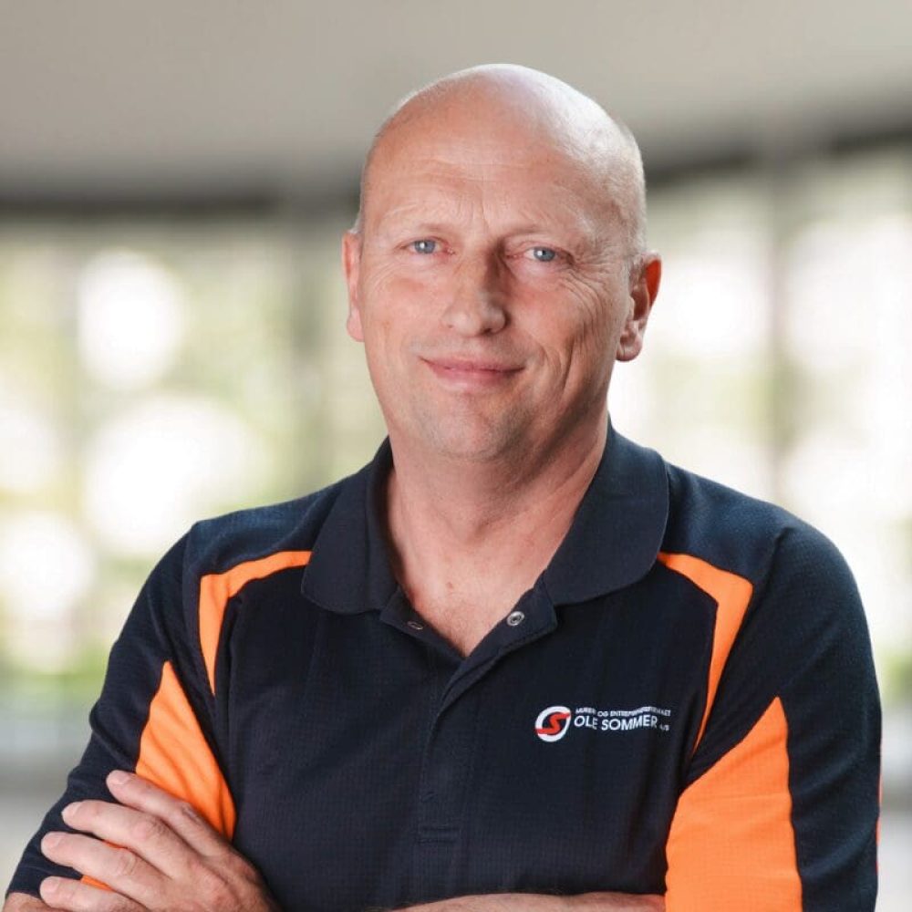 Portrætfoto af Kenneth Reichstein Hansen iført en sort og orange polo med Ole Sommer logo