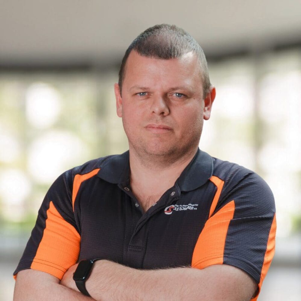 Portræt af Mick Laursen med armene over kors iført en sort og orange poloshirt